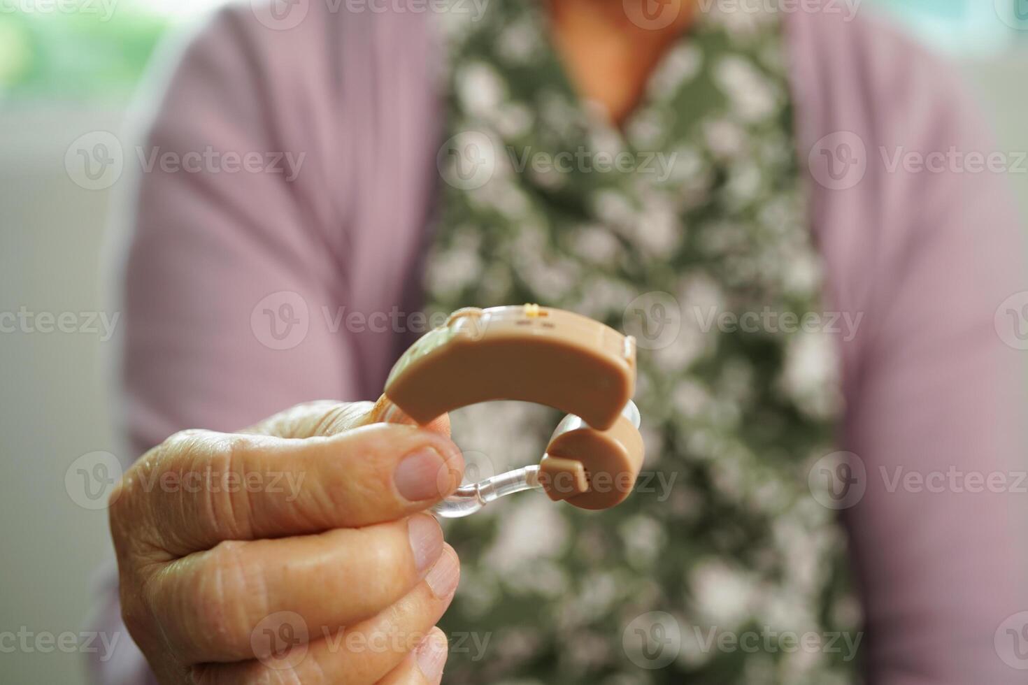 Aziatisch senior vrouw geduldig gebruik makend van horen steun in oor naar verminderen horen verlies probleem. foto