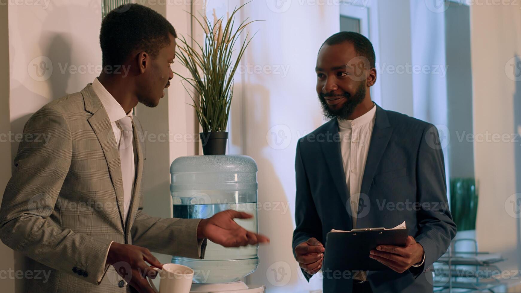 vrolijk Afrikaanse Amerikaans zakenlieden genieten van mooi hoor water tank gesprek gedurende nachtdienst pauze. blij arbeider hebben kop van koffie ontspannende terwijl communiceren met collega in kantoor foto