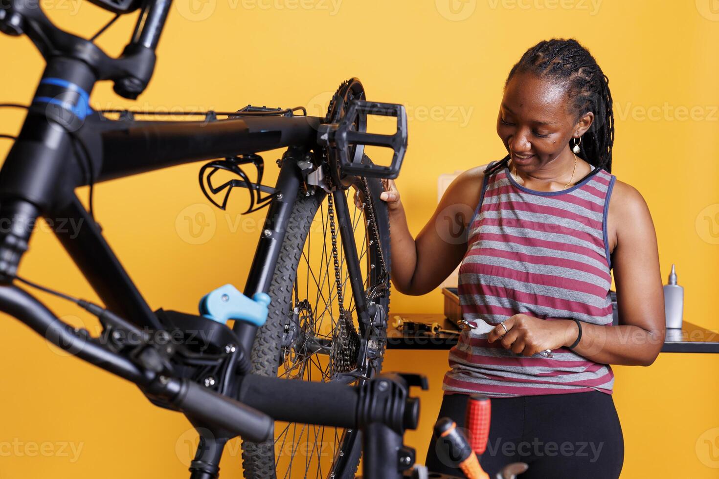 energiek Afrikaanse Amerikaans dame vakkundig reparaties haar fiets wiel met gespecialiseerd hulpmiddelen. gezond toegewijd zwart vrouw grondig inspecteren en repareren fiets band tegen geïsoleerd achtergrond. foto