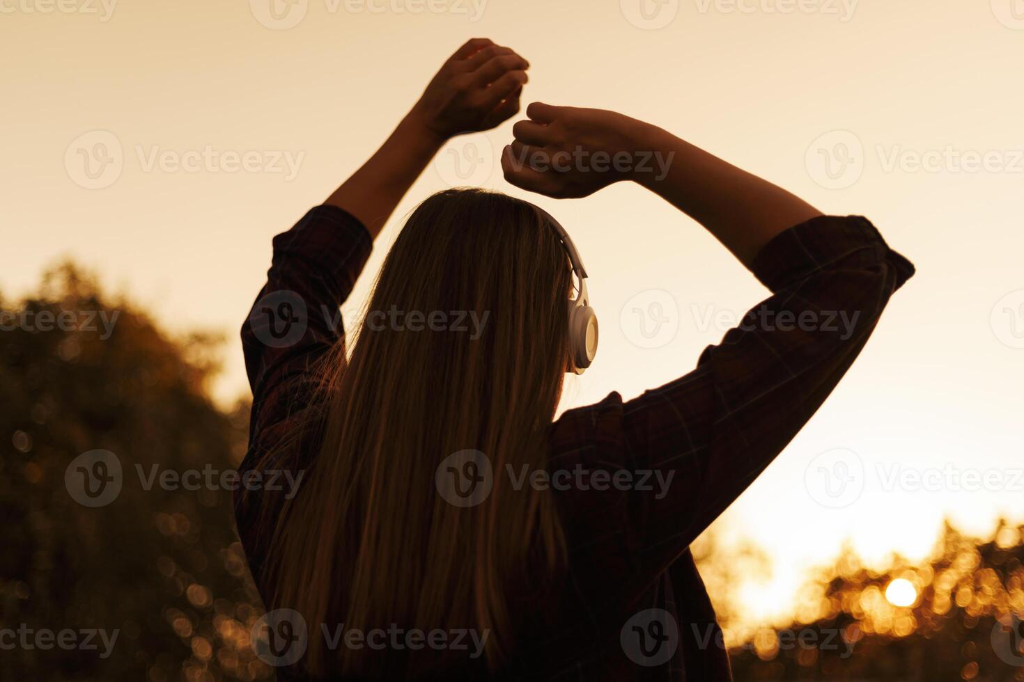silhouet van jong vrouw in hoofdtelefoons genieten van muziek- en dansen Bij zonsondergang foto