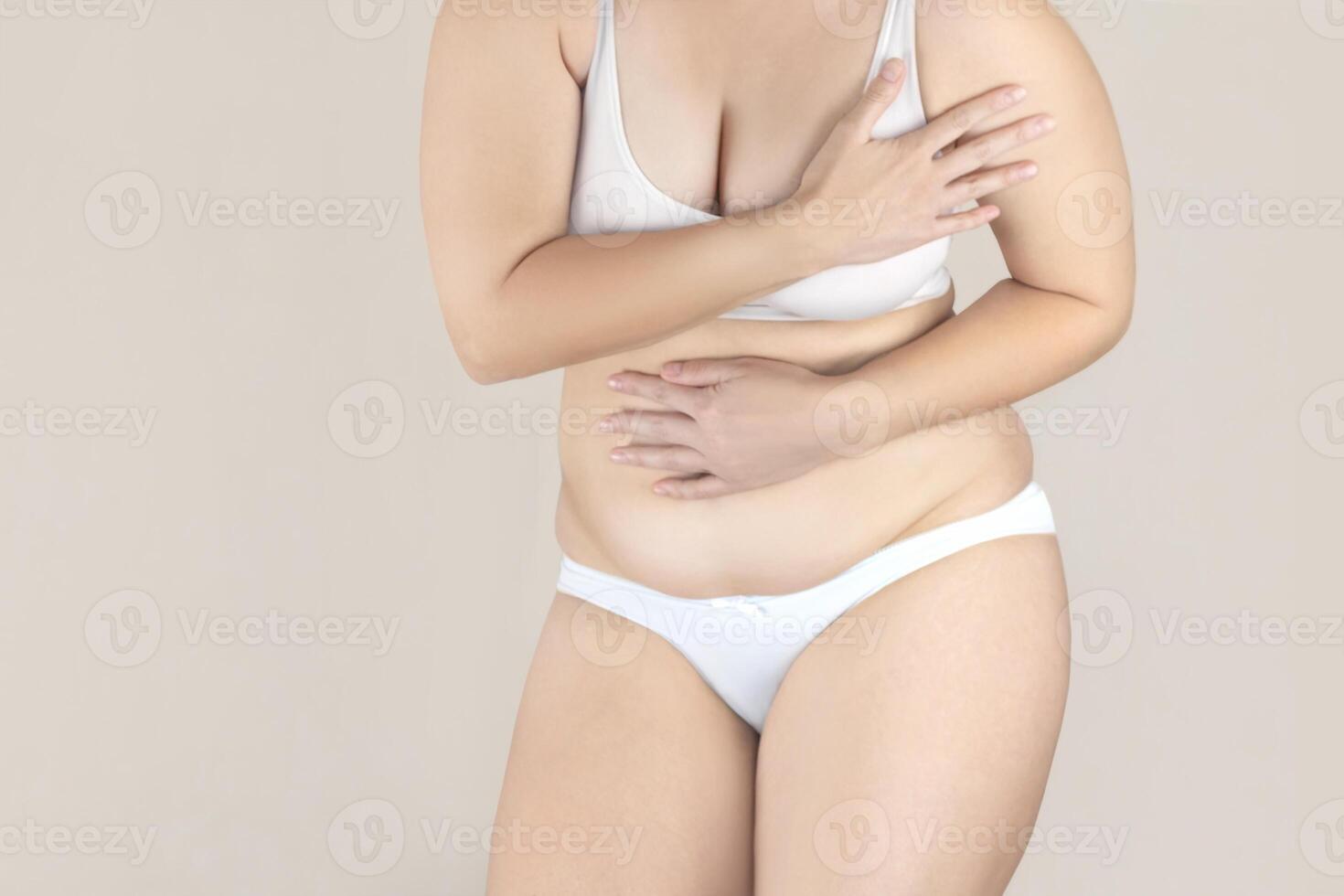 mollig vrouw met overschot dik in wit lingerie is in verlegenheid gebracht over haar lichaam, aan het bedekken omhoog foto