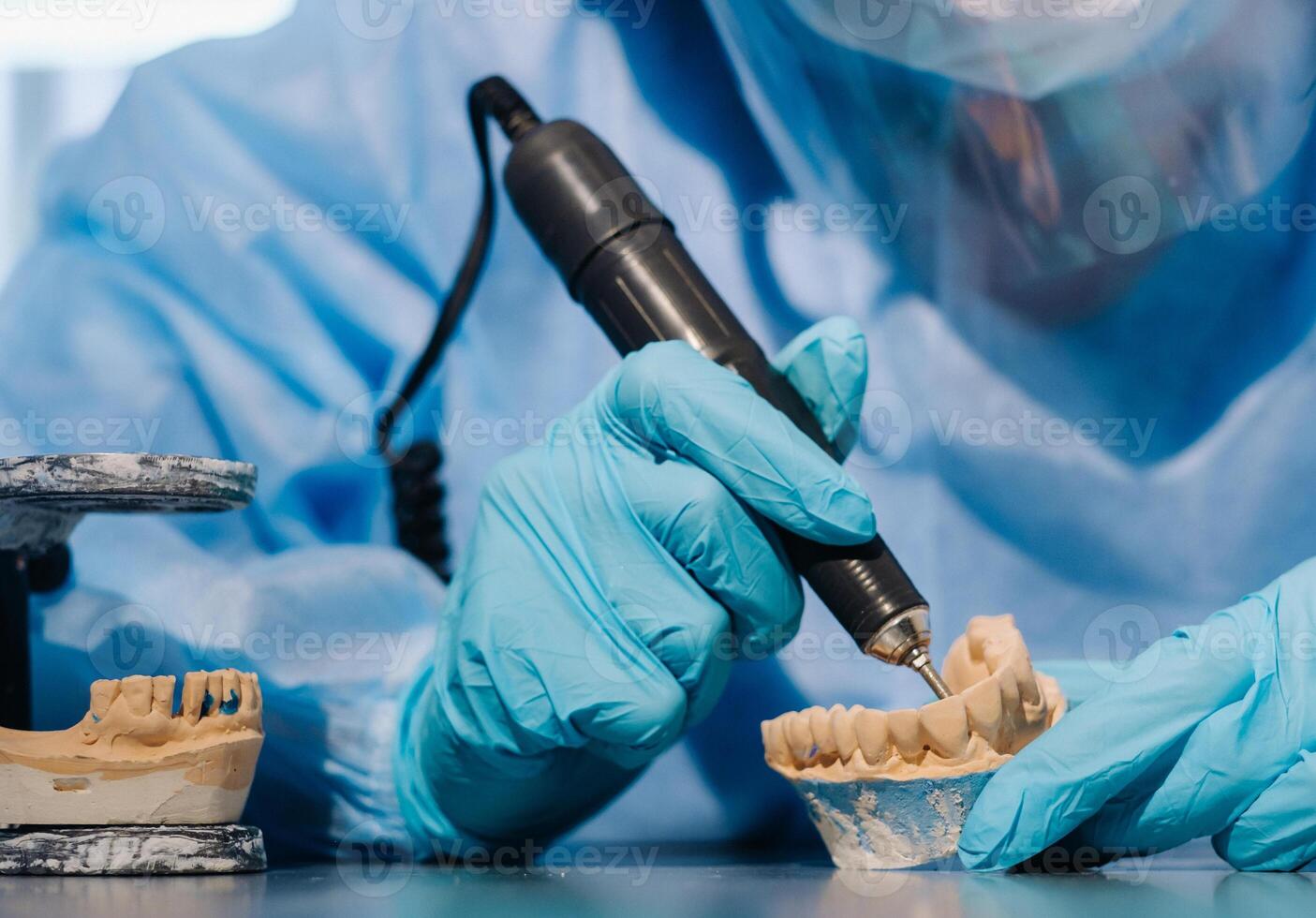 een gemaskeerd en gehandschoende tandheelkundig technicus werken Aan een prothetisch tand in zijn laboratorium foto