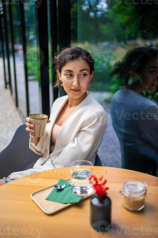 jong bedrijf vrouw Holding en drinken koffie in straat cafe in stad. portret van mooi vrouw arbeider aan het wachten cliënt Aan straat van Praag foto