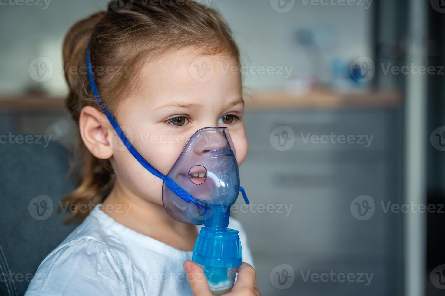 schattig weinig meisje zijn zittend en Holding een vernevelaar masker leunend tegen de gezicht, luchtweg behandeling concept foto