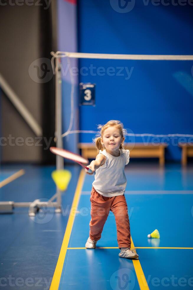 weinig meisje drie jaren oud spelen badminton in sport slijtage Aan binnen- rechtbank foto