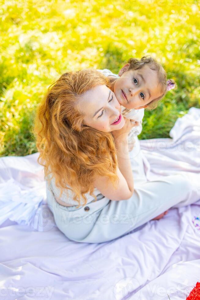 mam en dochter lachend en knuffelen zittend Aan een deken in de park de concept van een gelukkig familie, vriendschap, en liefde. foto