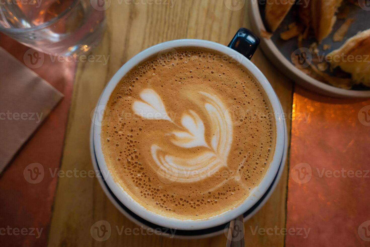 latte kunst en koffie cups met kaneel Aan de tafel, vergezeld door schotel, lepel, en suiker een verrukkelijk ochtend- drank tafereel Bij de cafe foto