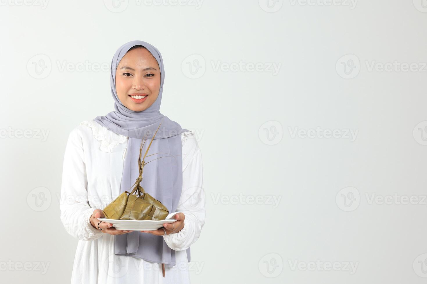 Indonesisch vrouw Holding wit bord met rijst- taart met diamant vorm voor moslim feestelijk foto