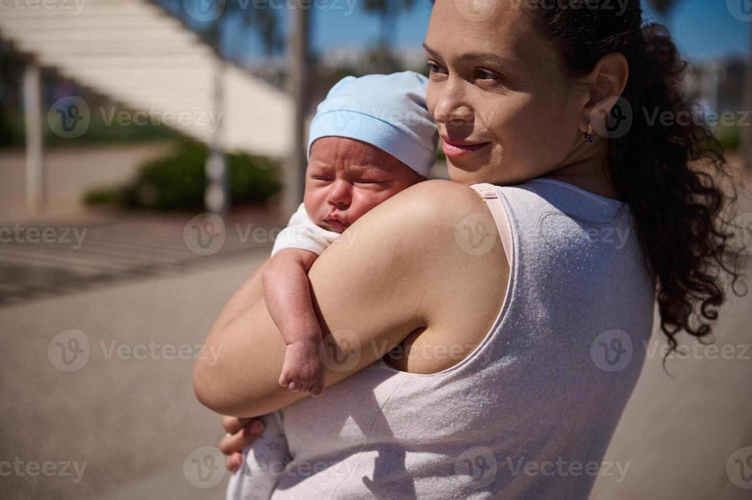 vrouw draag- haar pasgeboren baby terwijl wandelen samen Aan de stad Aan warm zonnig dag foto