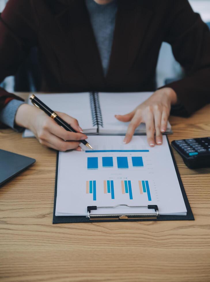 Aziatische zakenvrouw die een laptopcomputer gebruikt en op kantoor werkt met een rekenmachinedocument op het bureau, planning analyseert van het financiële rapport, businessplaninvestering, financiële analyseconcept. foto