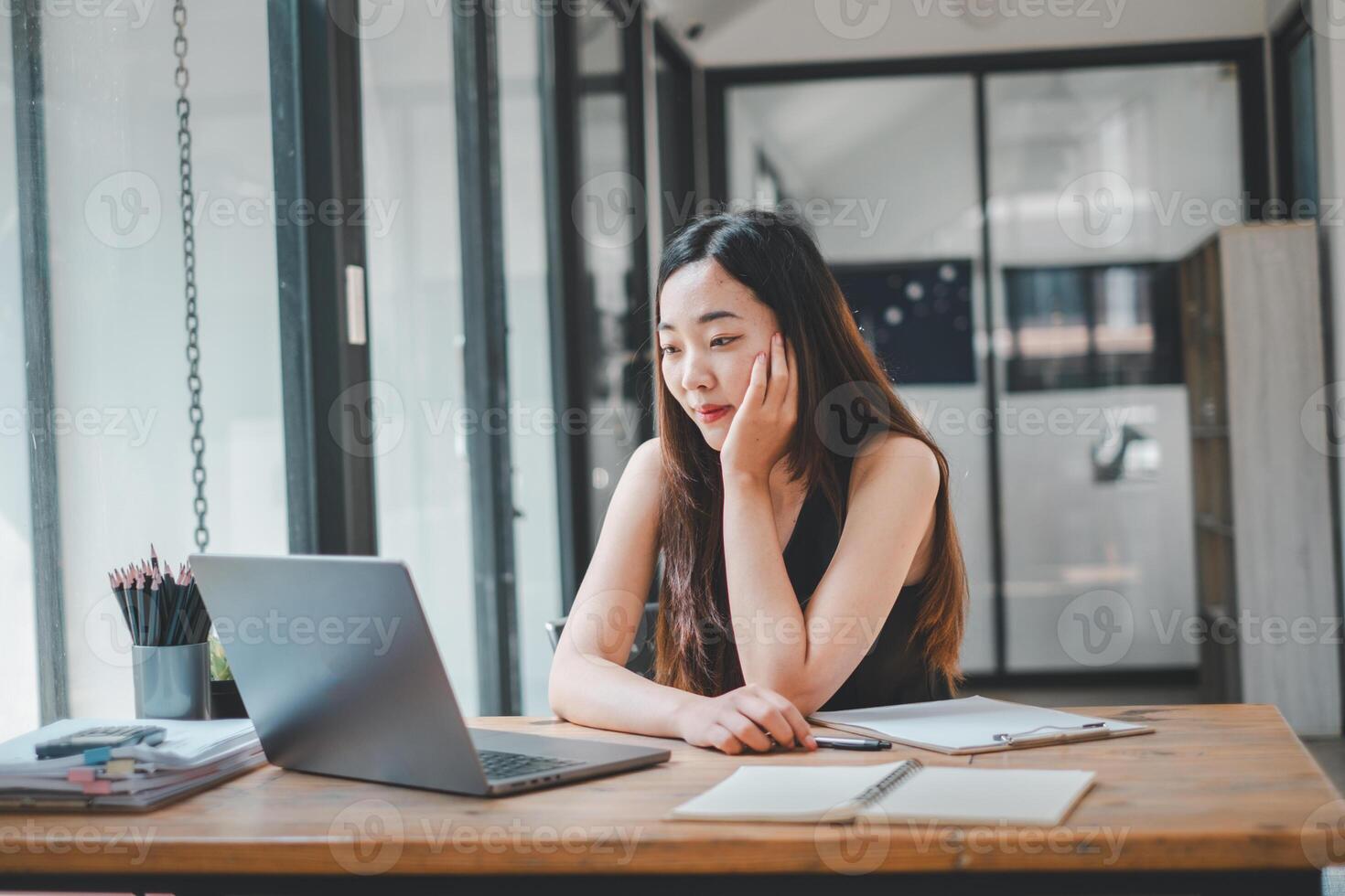 een jong freelancer concentraten Aan haar laptop scherm, ondergedompeld in haar werk Bij een houten bureau in een helder huis kantoor, een portret van toewijding en modern ondernemerschap. foto