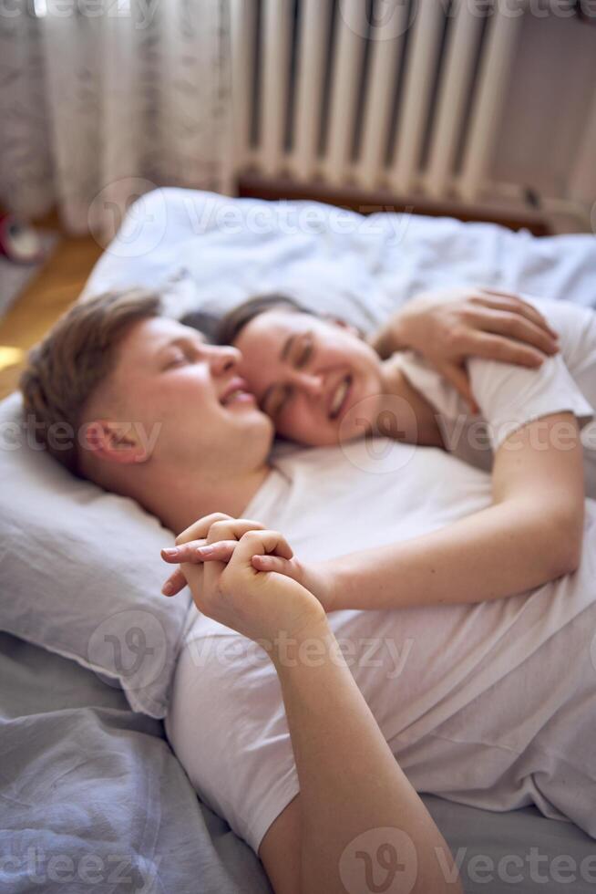 jong paar Aan de bed Holding handen, een meisje Aan een jongens schouder, inschrijving knuffels en accenten foto