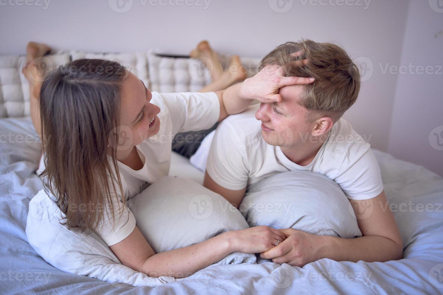 een jong mooi paar knuffelen en zoenen in bed, welzijn Bij huis foto