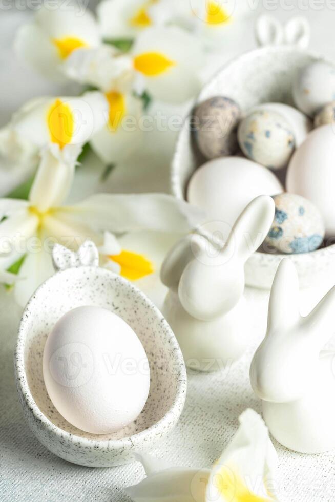 Pasen eieren in marmeren kommen met konijn oren, klein keramisch konijntjes, wit iris bloemen Aan wit. foto