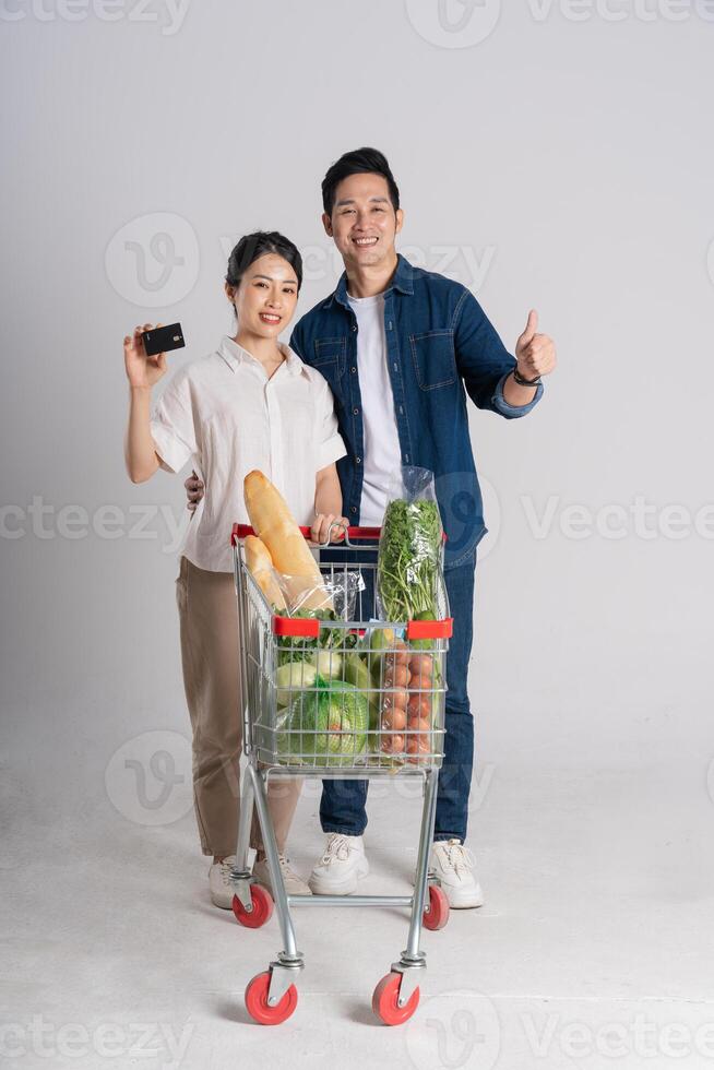 beeld van Aziatisch paar voortvarend supermarkt kar terwijl winkelen, geïsoleerd Aan wit achtergrond foto