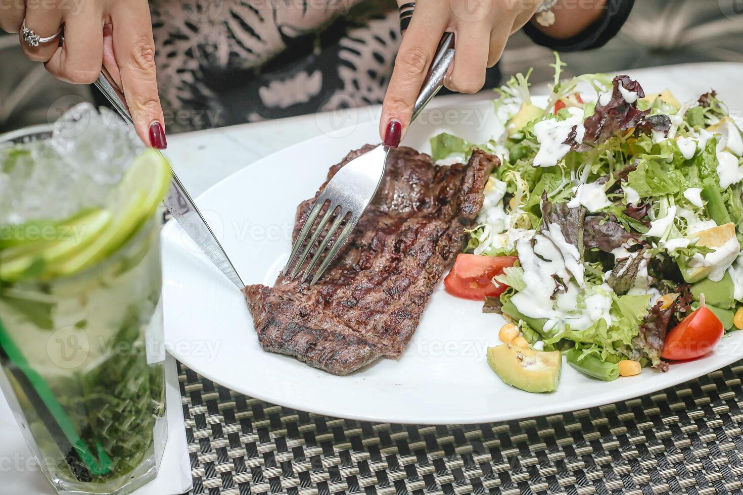 vrouw snijdend steak met mes en vork Bij restaurant tafel foto
