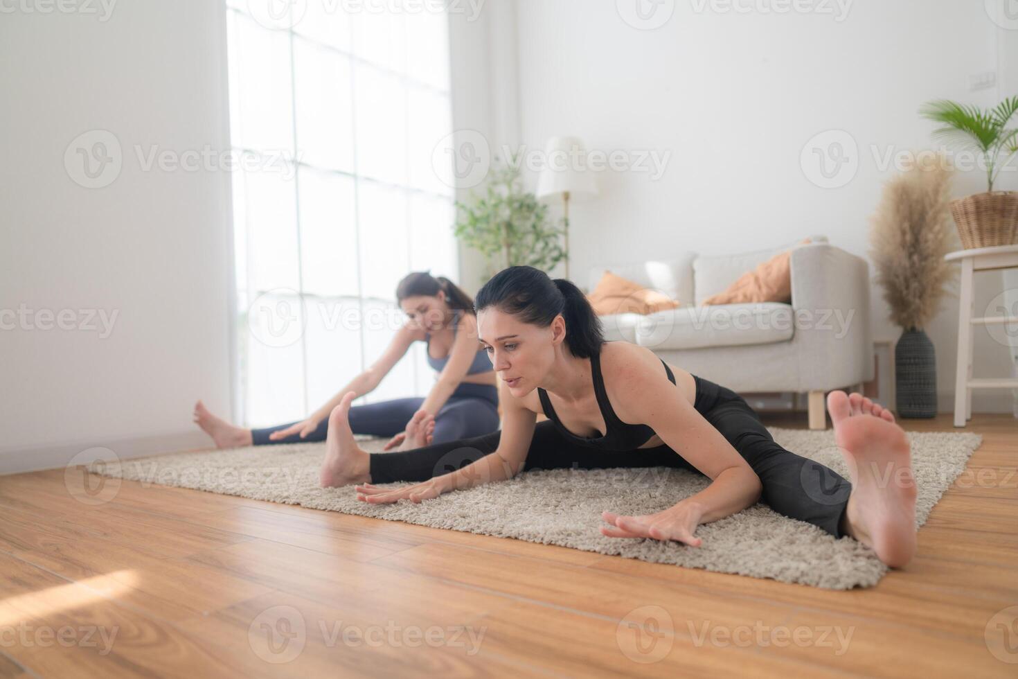 twee Dames zelfverzekerd opleiding yoga. atletisch Dames in sportkleding aan het doen geschiktheid uitrekken opdrachten Bij huis in de leven kamer. sport en recreatie concept. yoga leraar is helpen jong vrouw. foto