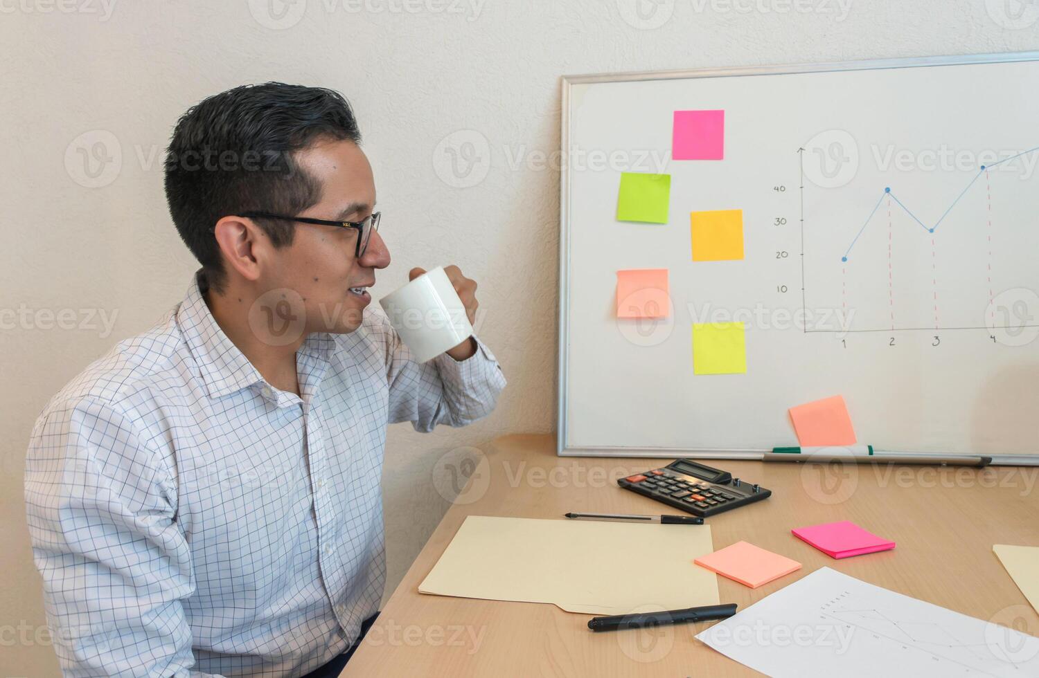 een Mens zittend Bij een bureau drinken van een wit mok foto