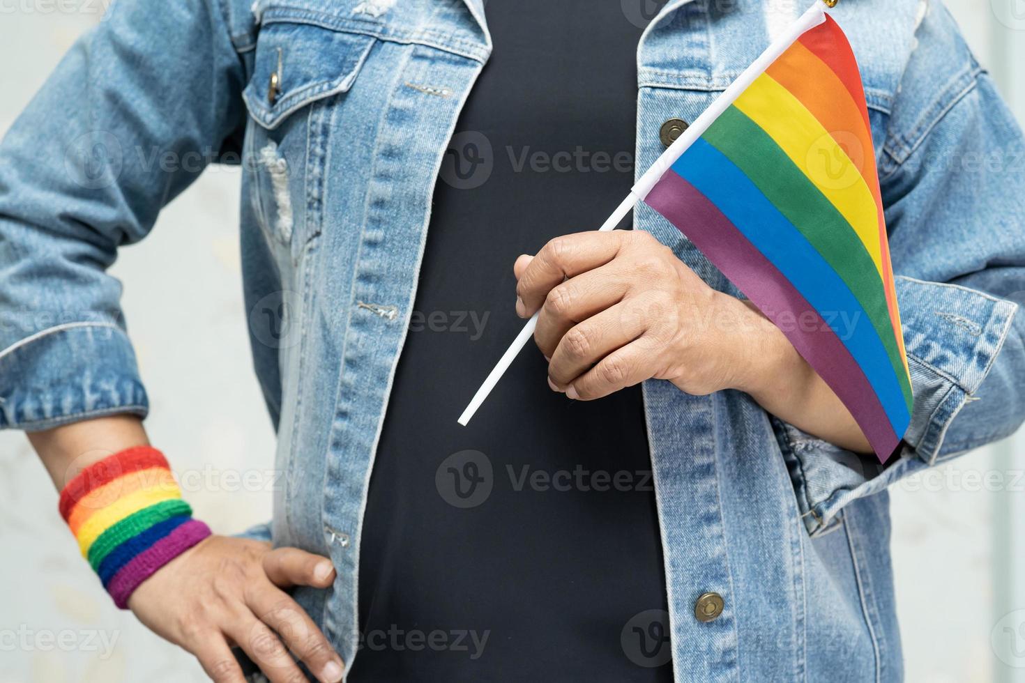 aziatische dame die een blauw spijkerjack of een denimoverhemd draagt en een regenboogvlag vasthoudt, symbool van de lgbt-trotsmaand viert jaarlijks in juni sociaal van homo, lesbienne, biseksueel, transgender, mensenrechten. foto