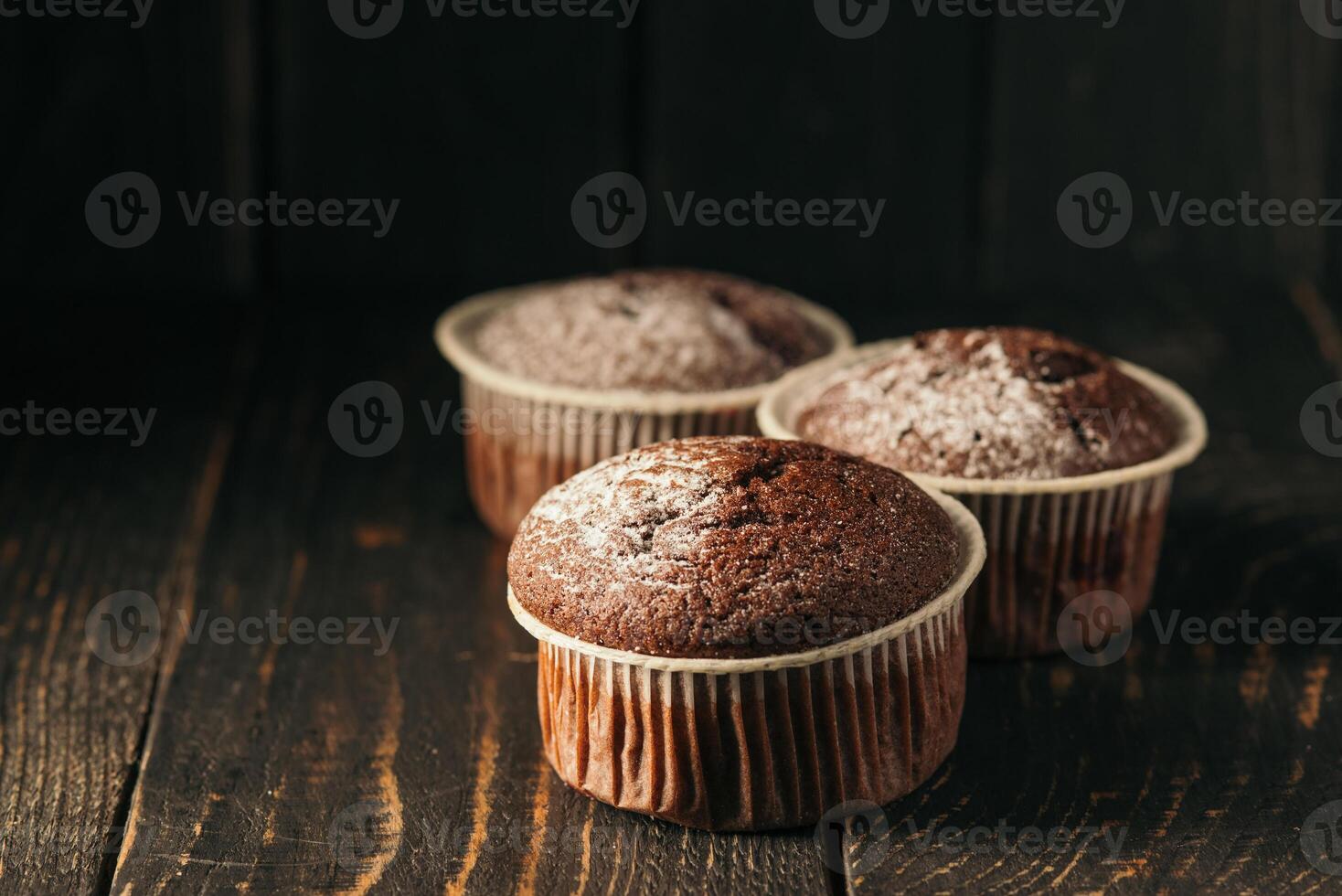 chocola muffins met gepoederd suiker Aan een zwart achtergrond. nog steeds leven dichtbij omhoog. donker humeurig. voedsel foto. foto