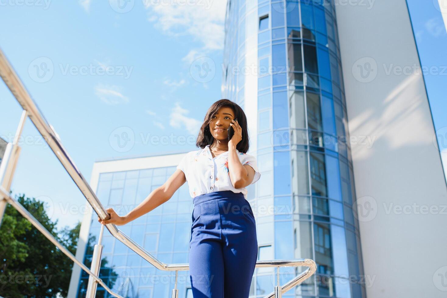 glimlachen Afrikaanse Amerikaans zakenvrouw gebruik makend van mobiel telefoon Aan straat tegen gebouw foto