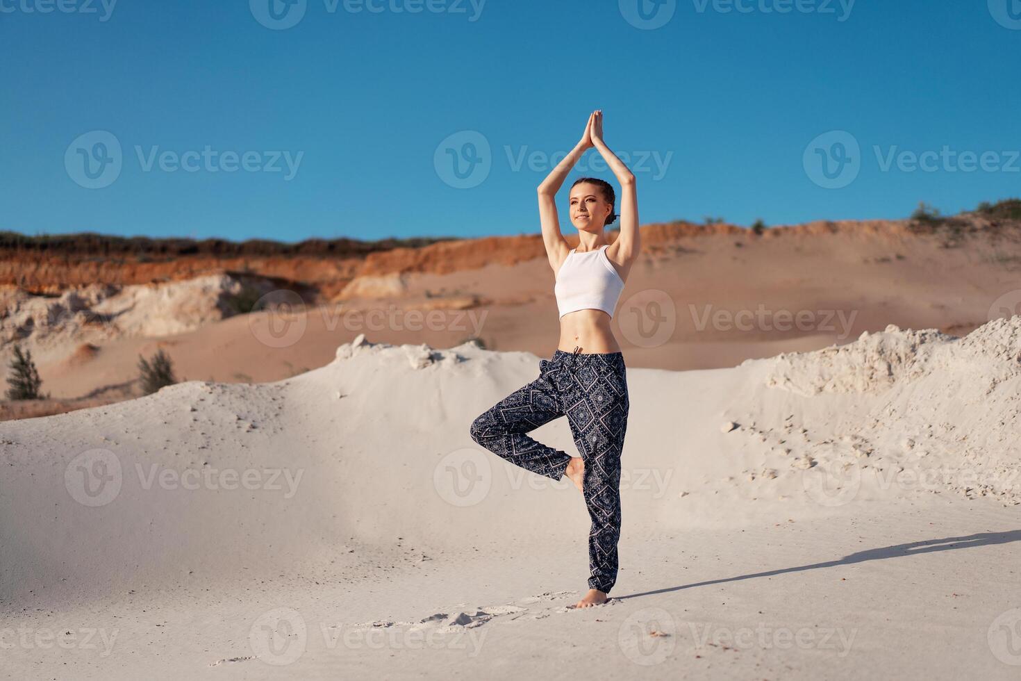 een mooi jong Kaukasisch meisje in een wit top en breed broek staan in een boom positie Aan de strand Aan de zand. foto