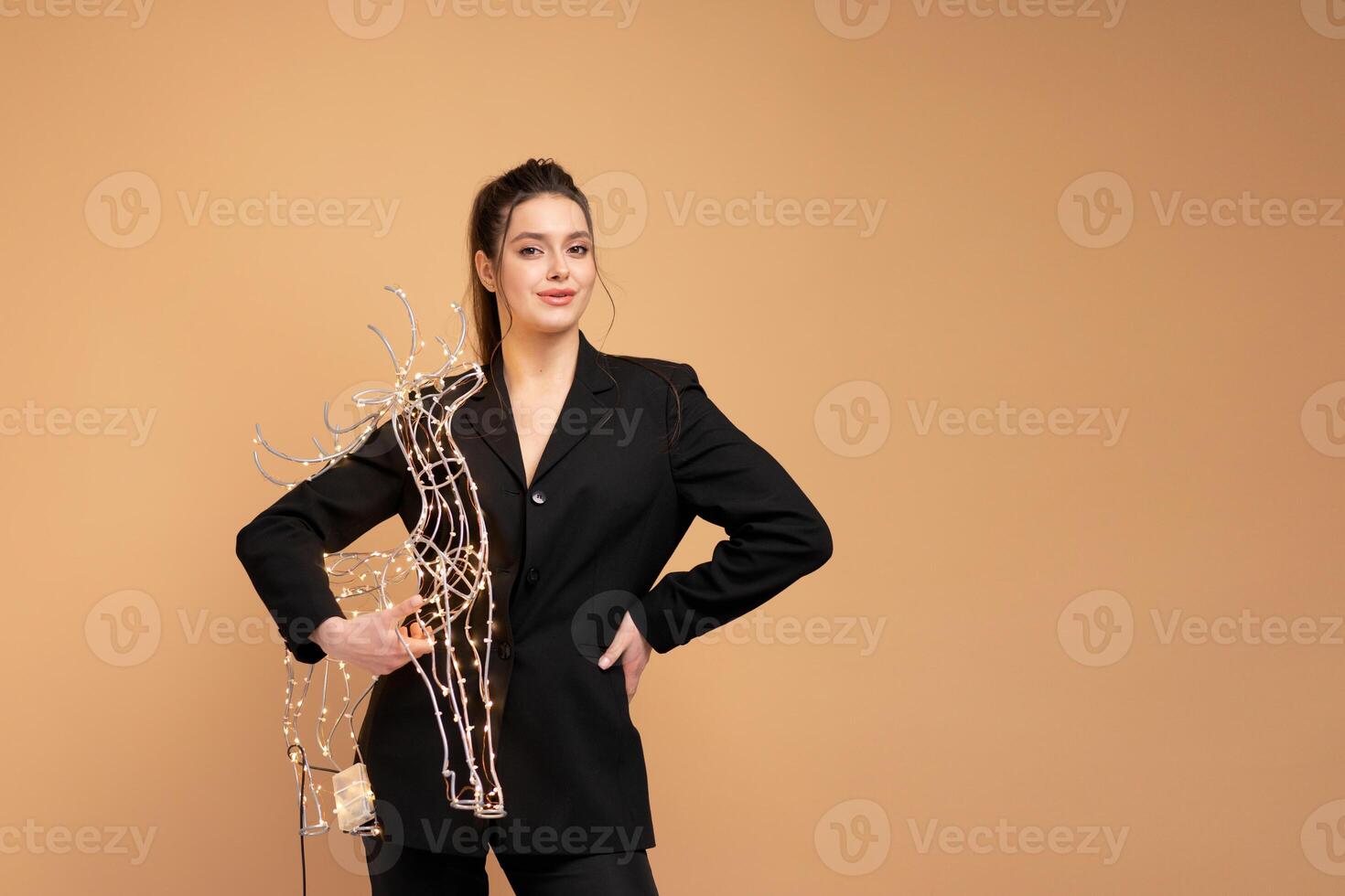 jong bedrijf vrouw Holding verlichte Kerstmis hert decor gekleed zwart pak geïsoleerd Aan pastel kleur achtergrond foto