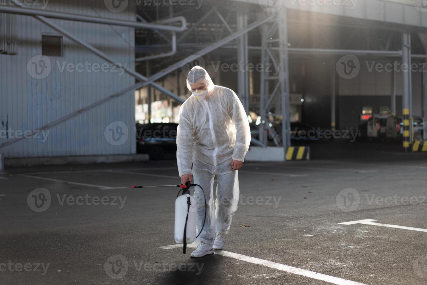 Mens gekleed wit beschermend overall sproeien oppervlakte antibacteriële ontsmettingsmiddel sproeier gedurende quarantaine foto