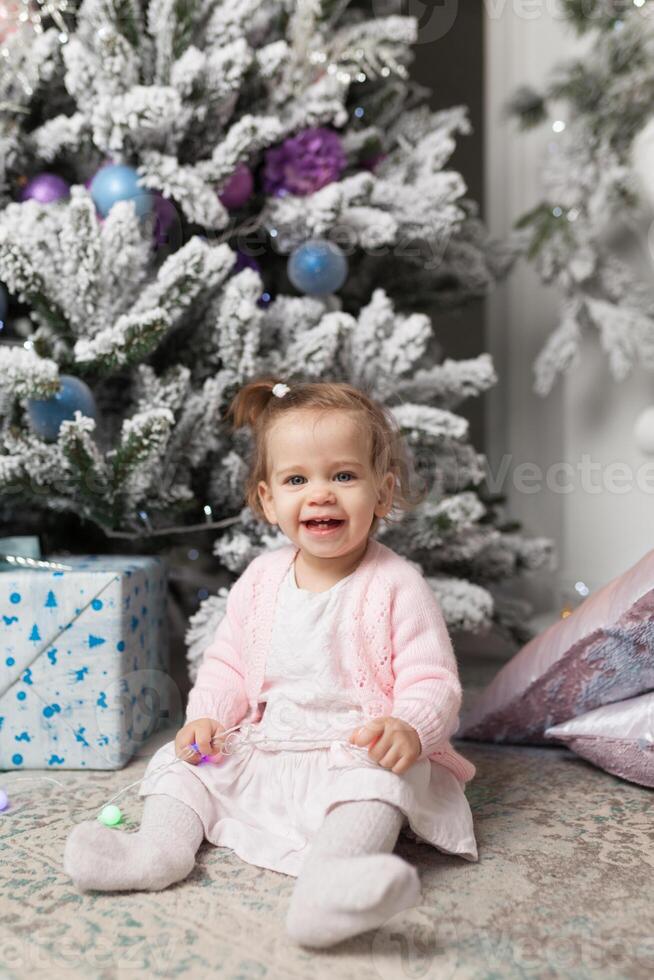 klein kind zittend in de buurt de Kerstmis boom foto