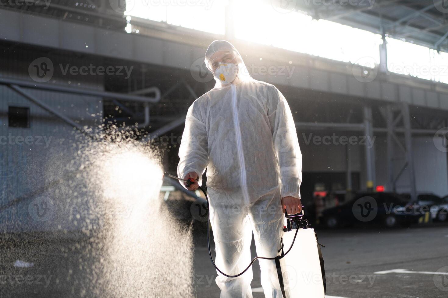 Mens gekleed wit beschermend overall sproeien oppervlakte antibacteriële ontsmettingsmiddel sproeier gedurende quarantaine foto