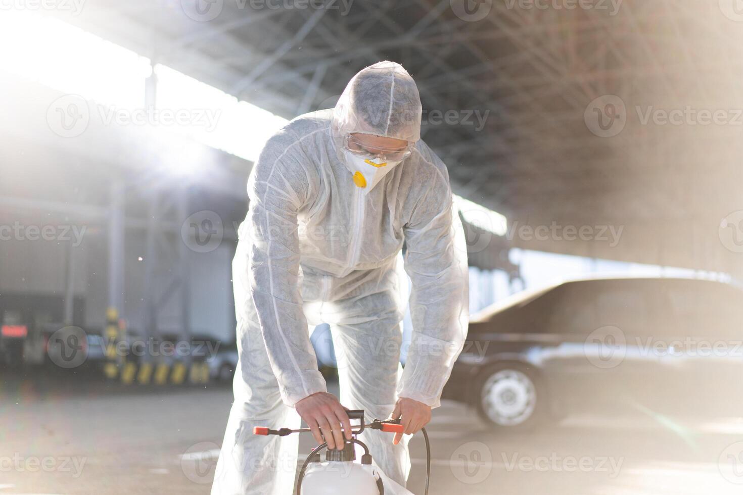 Mens gekleed wit beschermend overall sproeien oppervlakte antibacteriële ontsmettingsmiddel sproeier gedurende quarantaine foto