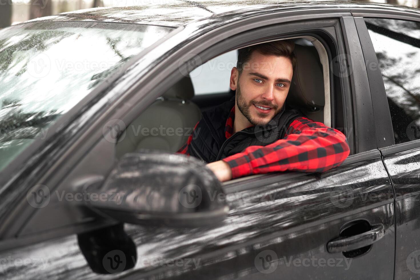 jong aantrekkelijk Kaukasisch Mens zit Bij de wiel van zijn auto zonnig winter dag. foto