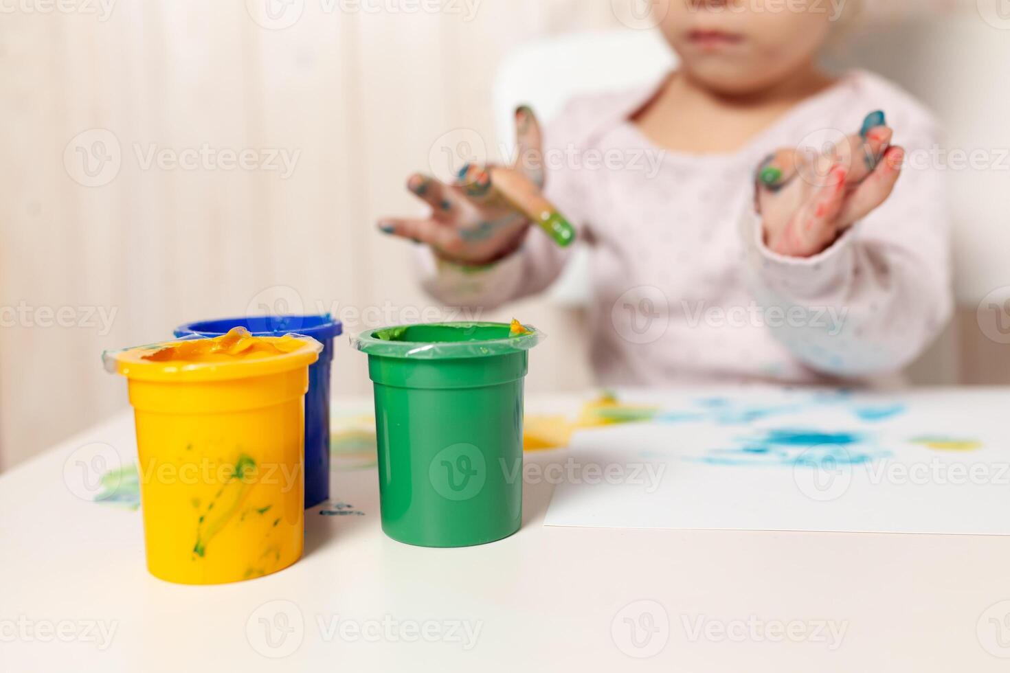 mooi weinig meisje trekt met vinger verven Aan een wit vel van papier. creatief kind ontwikkeling in kleuterschool of vrij tijd Bij huis foto