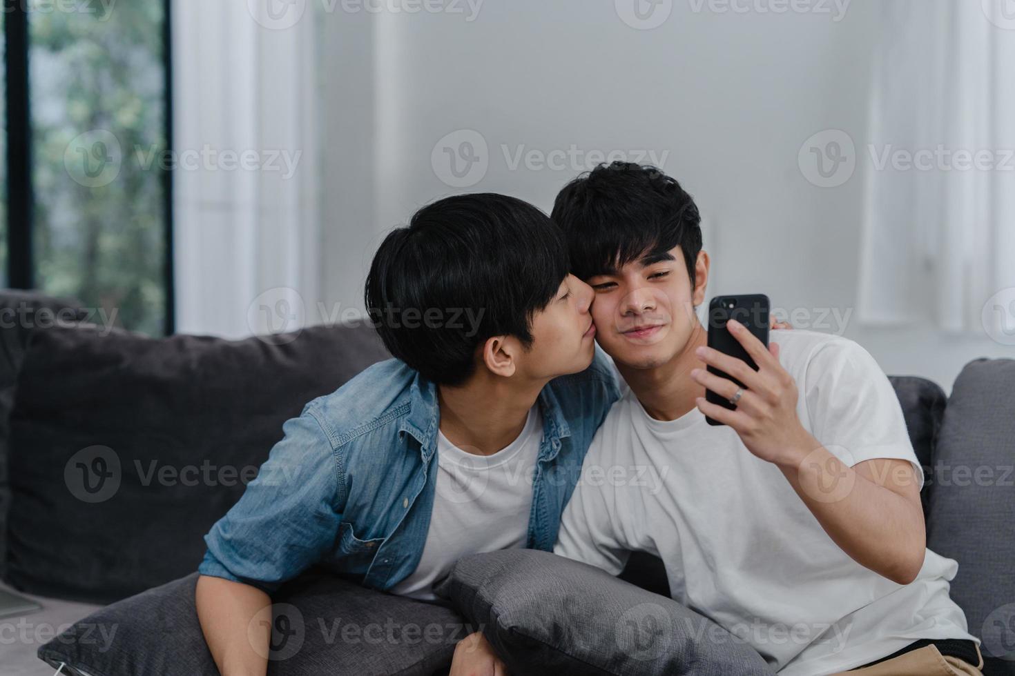 Aziatische influencer homopaar vlog thuis. aziatische lgbtq-mannen gelukkig ontspannen plezier met behulp van technologie mobiele telefoon opnemen lifestyle vlog video-upload in sociale media terwijl ze op de bank in het woonkamerconcept liggen. foto