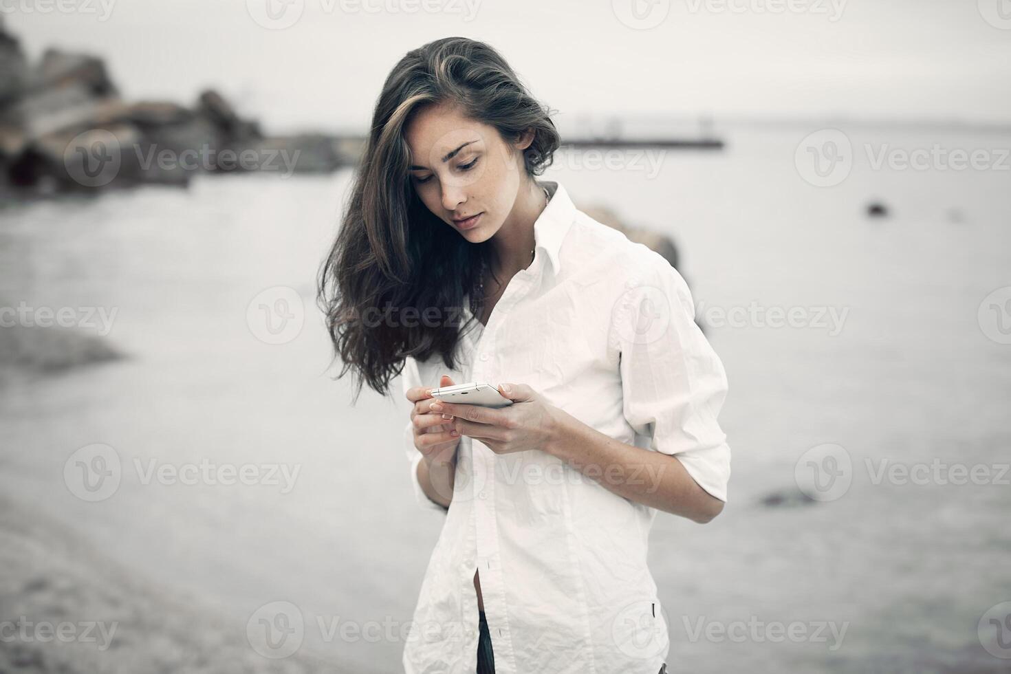 portret van tiener meisje wandelen Aan de strand is controle online de mobiel telefoon aan het wachten voor een bericht foto