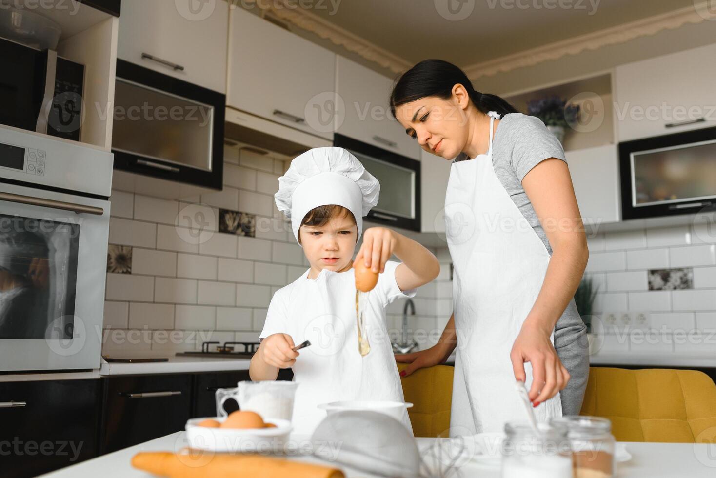 een jong en mooi moeder is voorbereidingen treffen voedsel Bij huis in de keuken, langs met haar weinig zoon foto