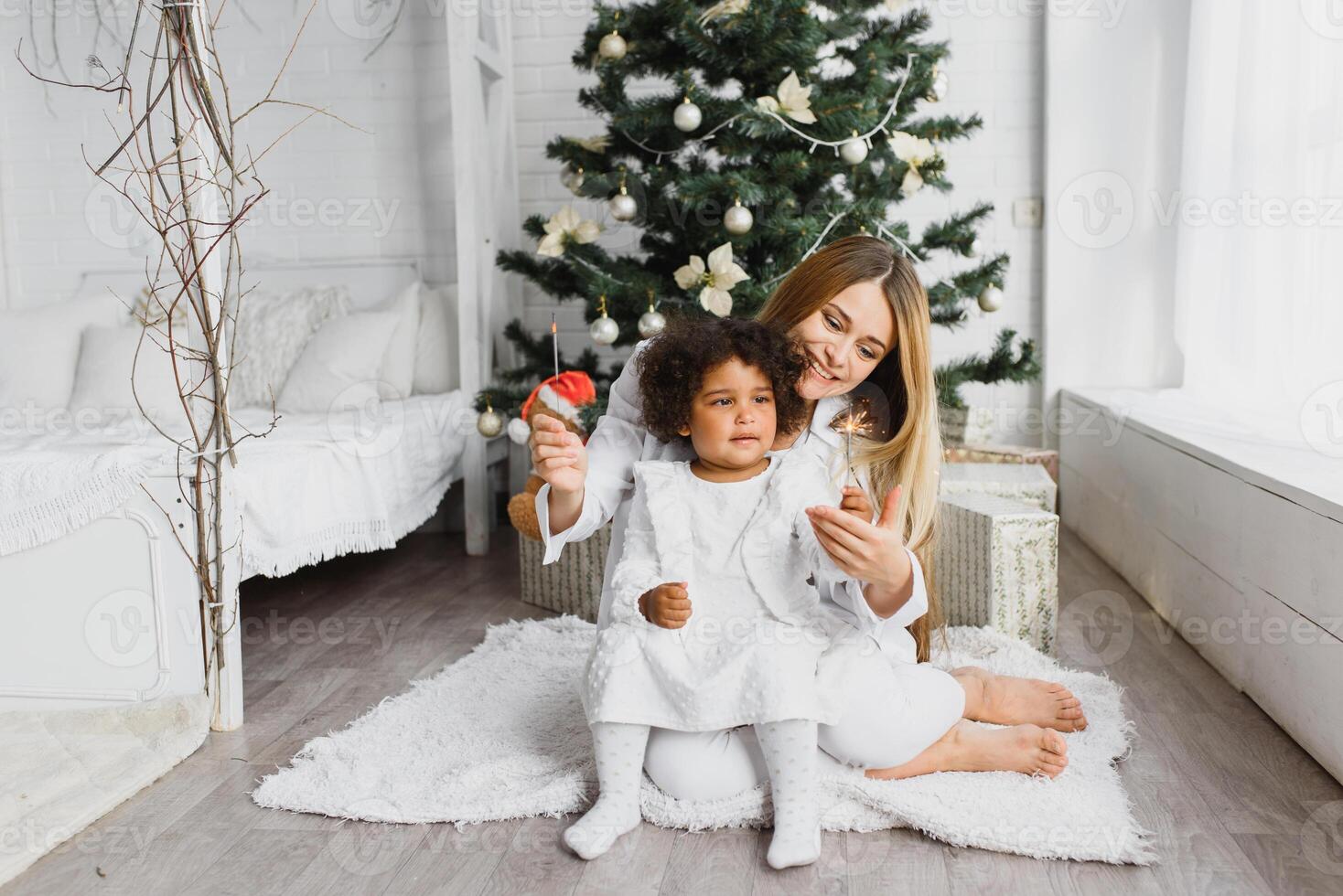 vrolijk Kerstmis en gelukkig vakantie vrolijk mam en haar schattig dochter Bij Kerstmis boom. ouder en weinig kind hebben pret in de buurt Kerstmis boom binnenshuis. liefhebbend familie met presenteert in kamer. foto