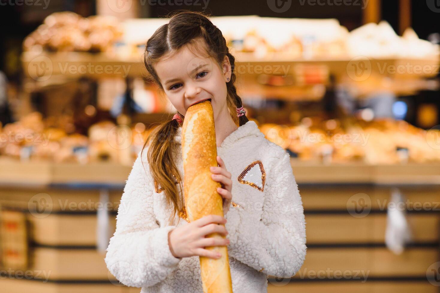jong en grappig meisje aan het eten stokbrood in voorkant van de bakkerij op te slaan foto