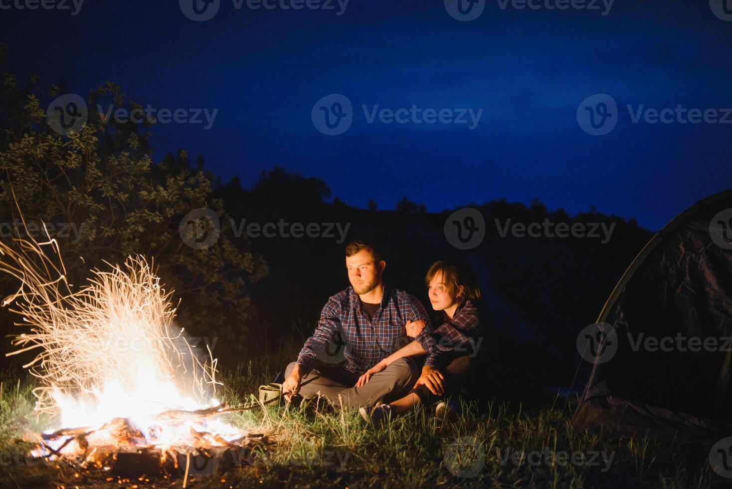 gelukkig romantisch paar reizigers resting Bij vreugdevuur in de buurt gloeiend toerist tent onder verbazingwekkend nacht lucht. de concept van actief recreatie en reizen met een tent foto