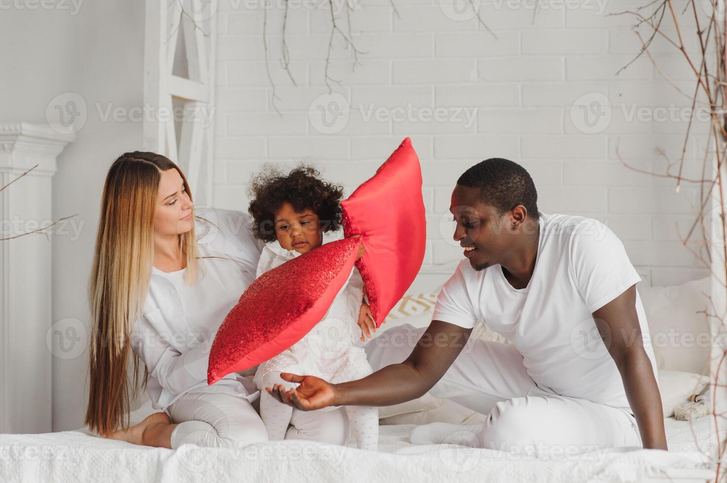 portret van gelukkig multiraciaal jong familie aan het liegen Aan knus wit bed Bij huis, glimlachen Internationale mam en vader ontspannende met weinig biraciaal meisje kind poseren voor afbeelding in slaapkamer foto