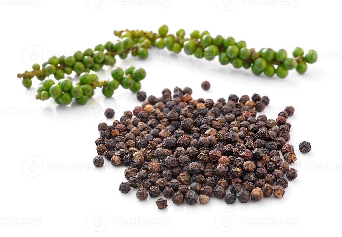 Zwarte peperkorrels en trossen verse groene peper geïsoleerd op een witte achtergrond foto
