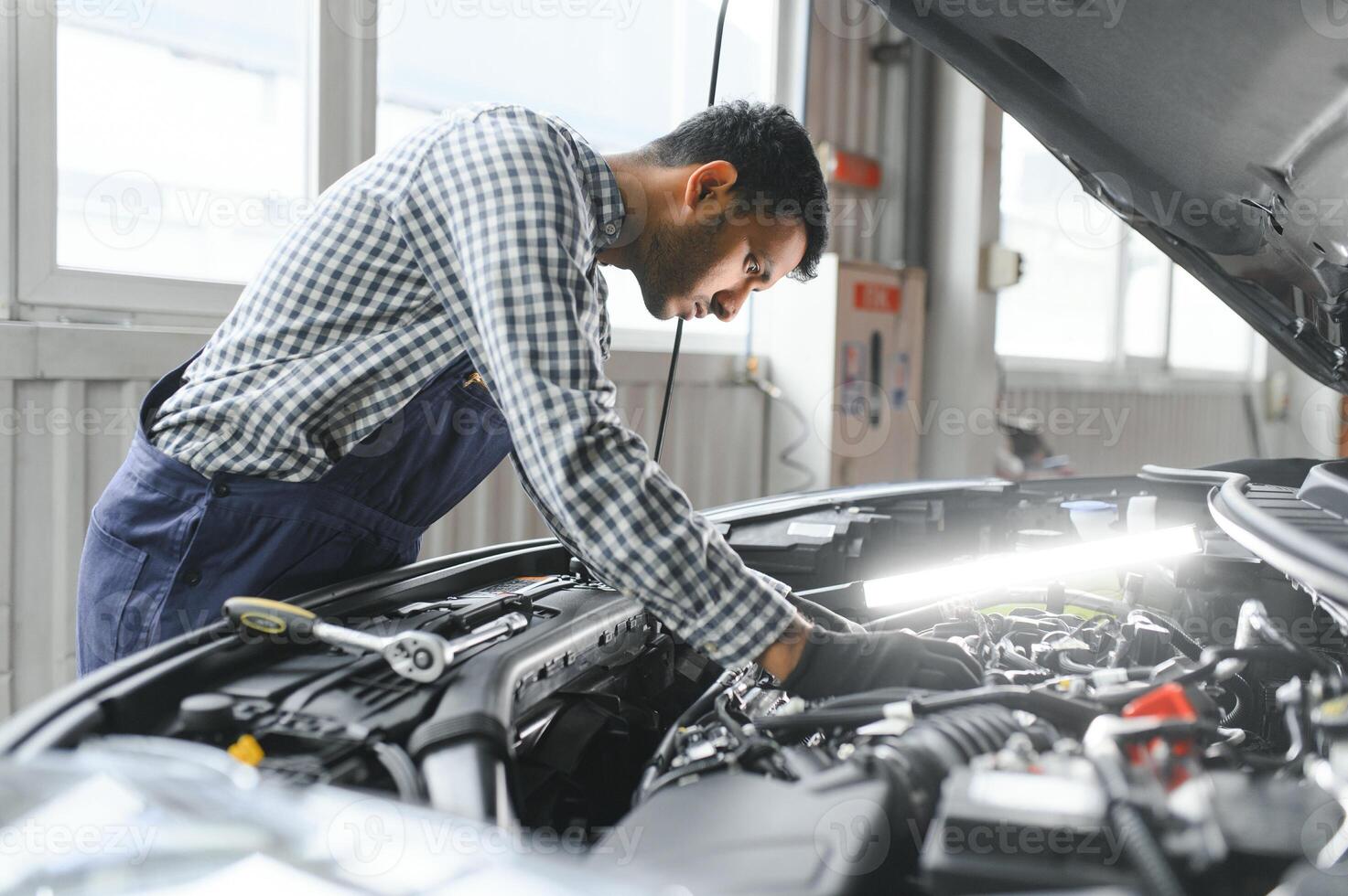 Latijns spaans auto monteur in uniform is onderzoeken een auto terwijl werken in auto onderhoud foto