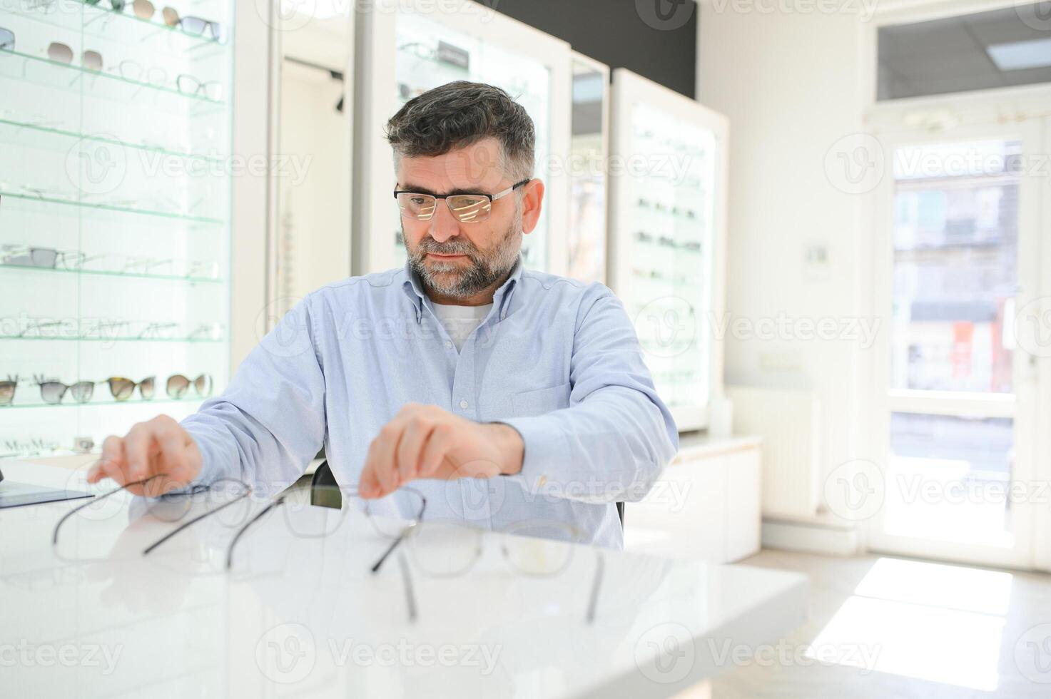 bril controleren, senior visie en ouderen Mens Bij een overleg plegen optometrie kliniek voor welzijn. Vrolijk, glimlach en oud gezicht met lens, kader en eyewear keuze in een op te slaan voor helpen krijgen een recept. foto