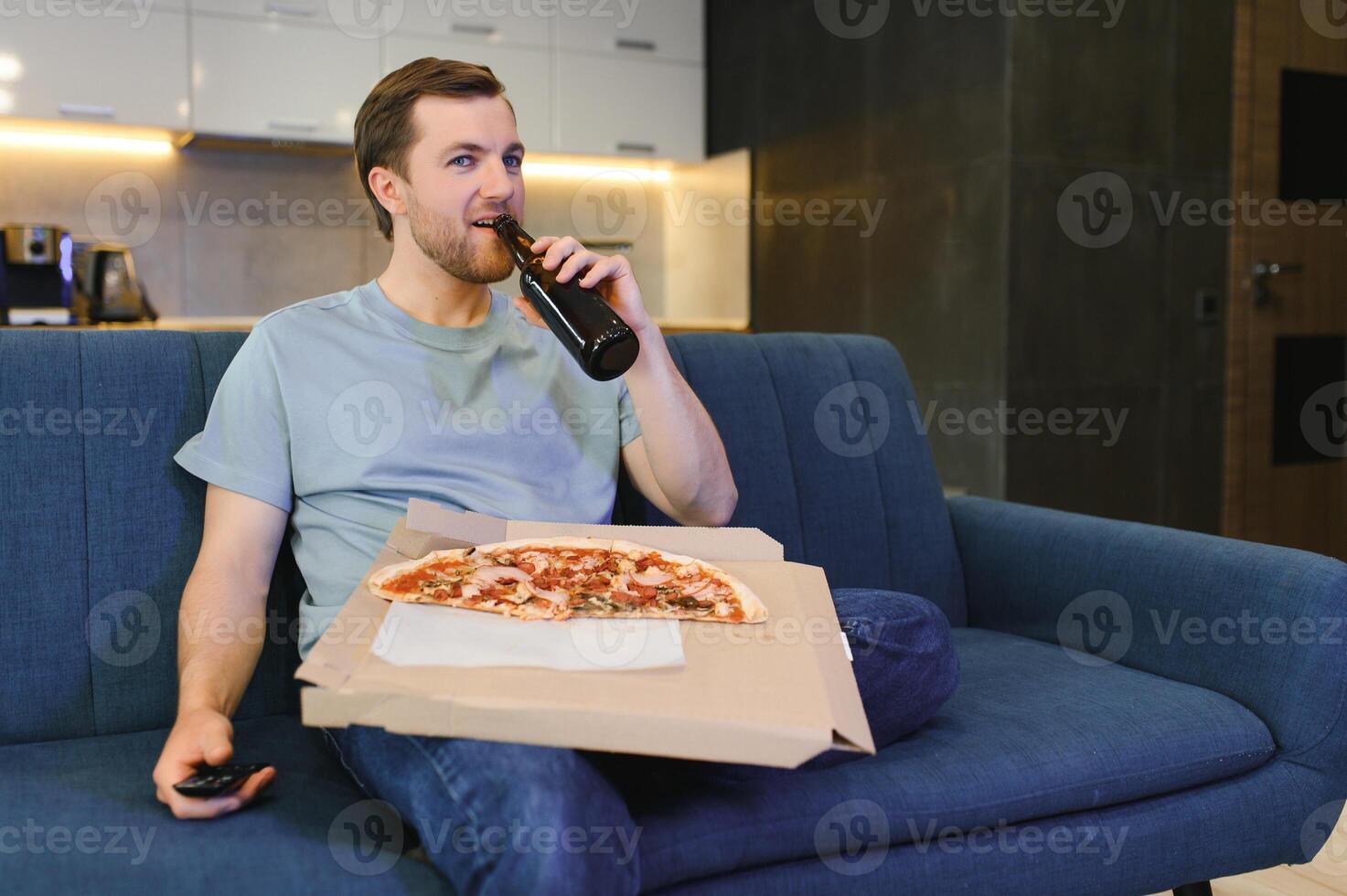 gelukkig jong Mens drinken bier en aan het eten pizza wanneer aan het kijken spel Aan TV Bij huis foto
