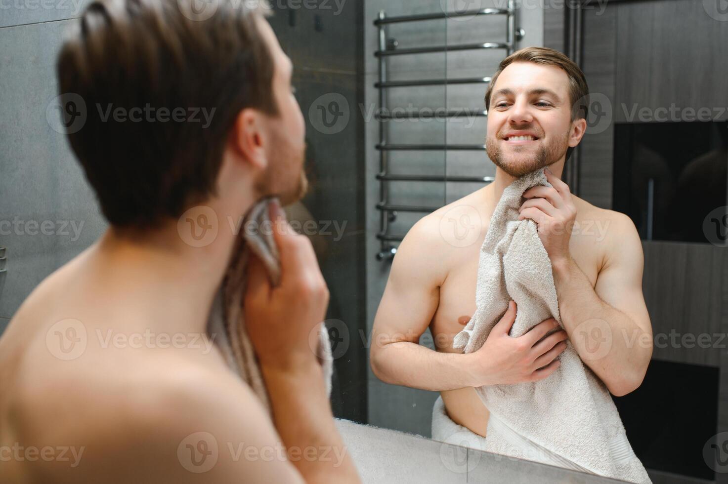 jong Kaukasisch Mens kijken in spiegel Doen huidsverzorging gelaats routine- na douche in huis badkamer, millennial mannetje in handdoek na bad van toepassing zijn gezicht lotion of room Aan huid na scheren, hygiëne concept. foto