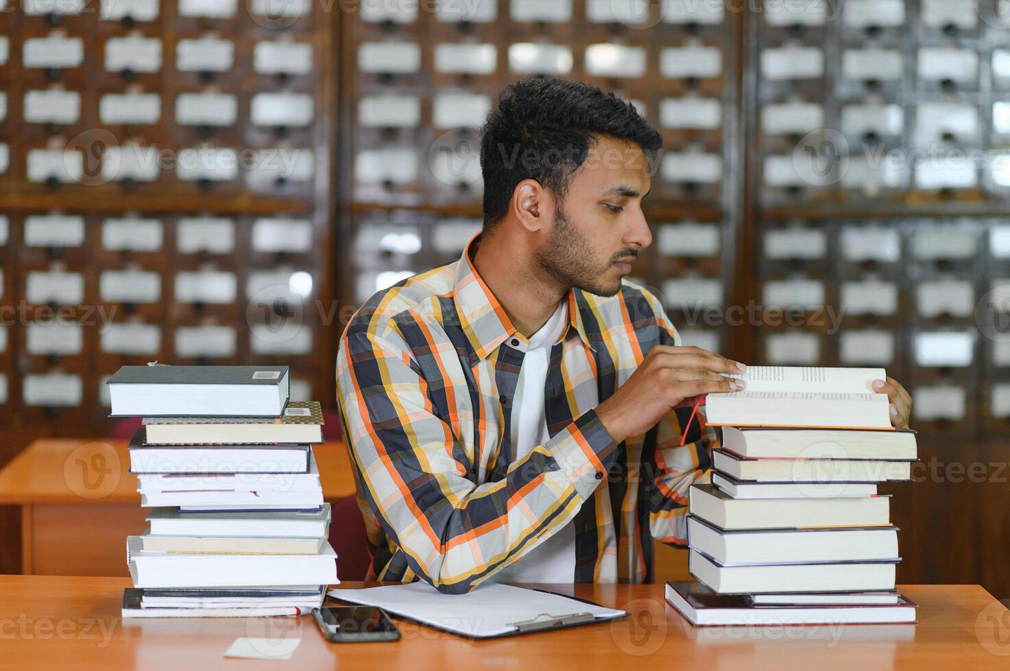 gelukkig slim Indisch of Arabisch jongen, gemengd ras mannelijk, Universiteit leerling, in de bibliotheek foto