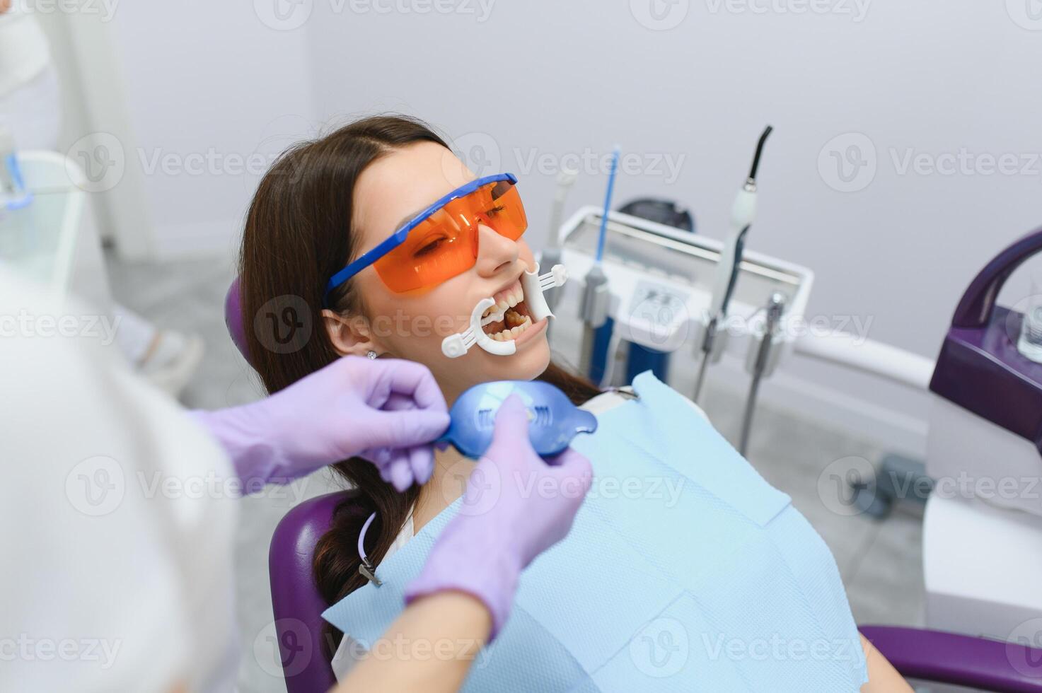 beeld van mooi jong vrouw zittend in tandheelkundig stoel Bij medisch centrum terwijl professioneel dokter vaststelling haar tanden foto