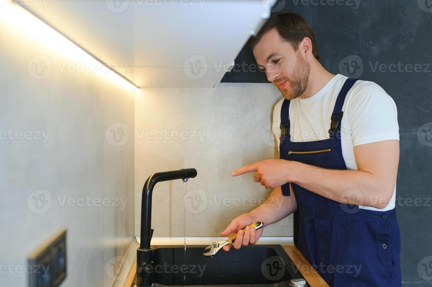 gelukkig jong mannetje loodgieter vaststelling kraan in keuken foto