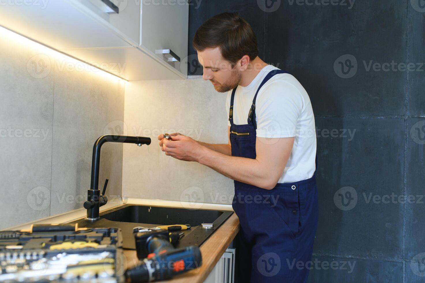 gelukkig jong mannetje loodgieter vaststelling kraan in keuken foto