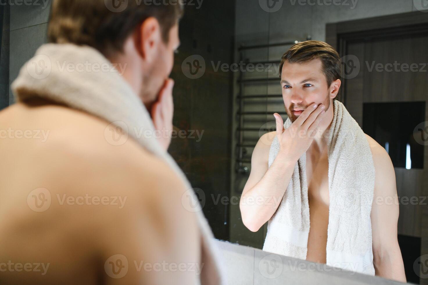 jong Mens op zoek in spiegel na scheren Bij huis foto